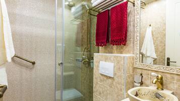 A bathroom with a glass-enclosed shower, a sink with a decorative basin, and two towels hanging on a rack.
