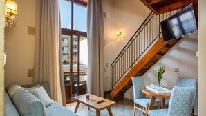 A living room with a sofa, a table, chairs, a TV mounted on the wall, and a staircase. - Phaedra Suites (Rethymno)