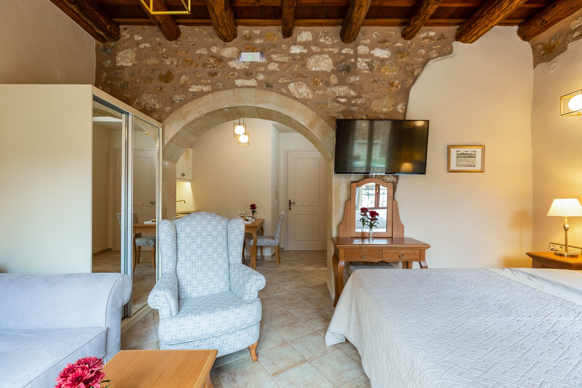 A cozy room with a stone ceiling, a bed, a chair, a desk, and a television.