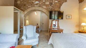 A cozy room with a stone ceiling, a bed, a chair, a desk, and a television.