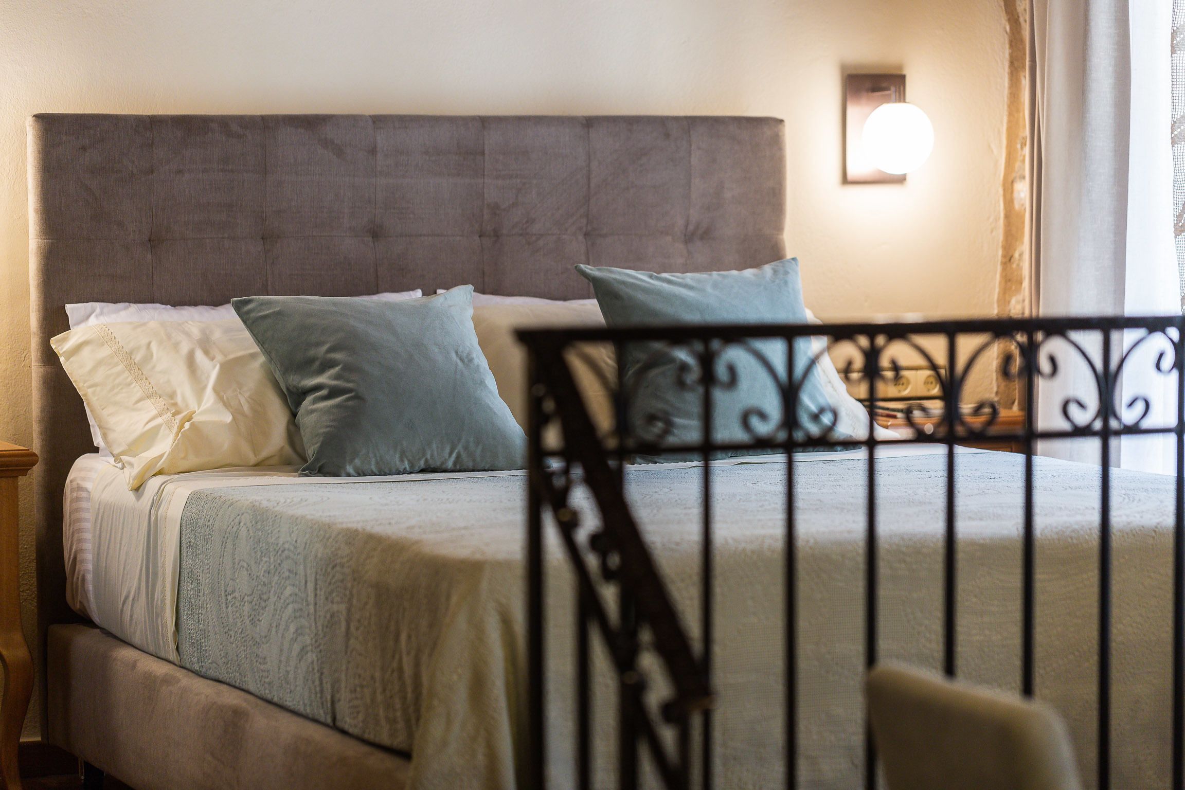 Una cama con cabecera tapizada de gris, colcha blanca y azul, y dos almohadas.