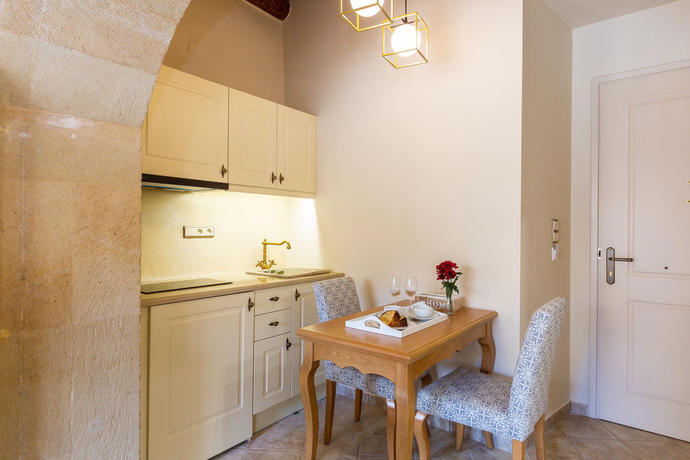 A compact kitchen with a wooden table and chairs, a white cabinet, and a hanging light fixture.