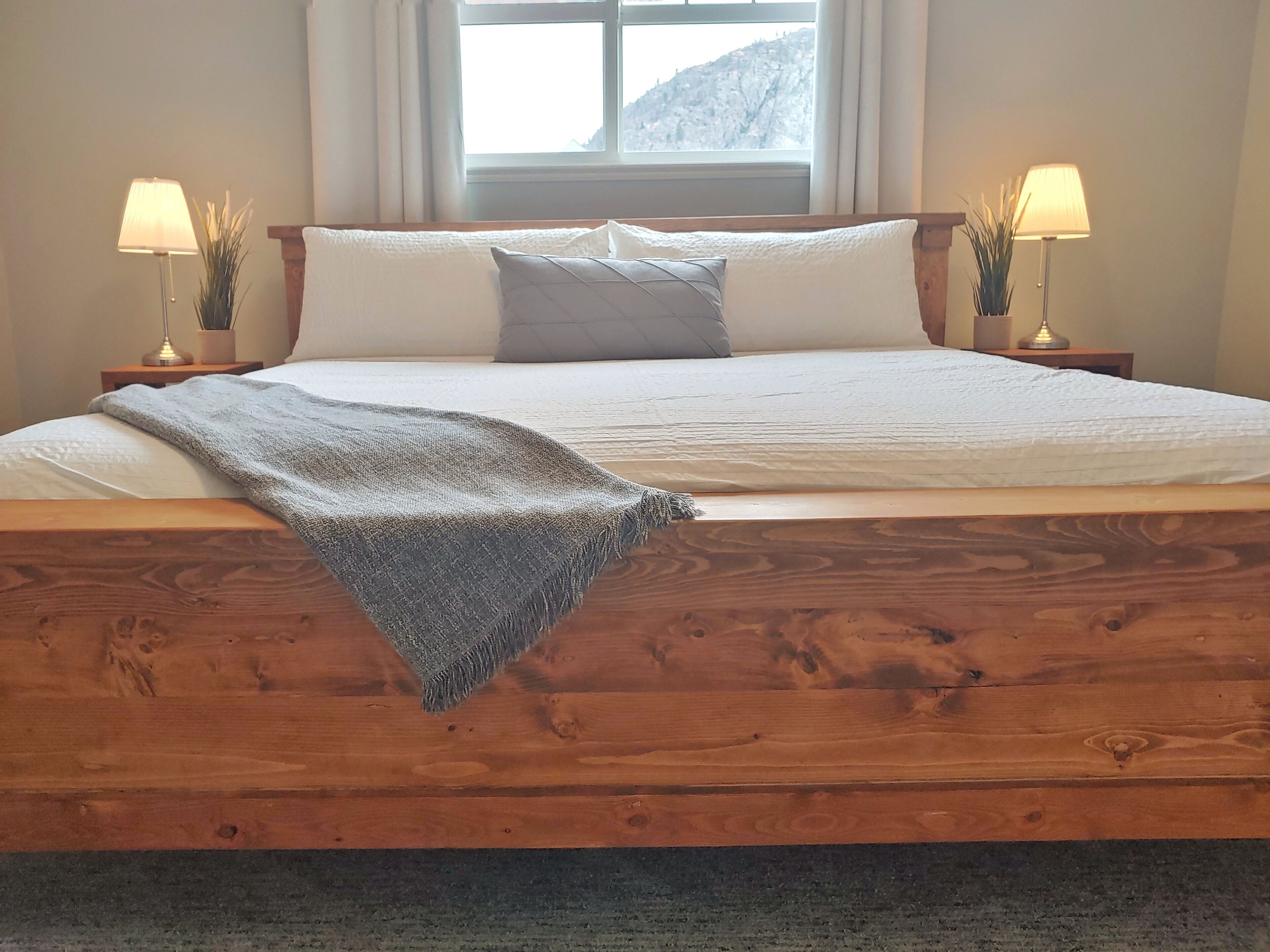 Un letto rifatto con cura, con una testiera in legno, due lampade sui comodini e una finestra con vista sulle montagne.