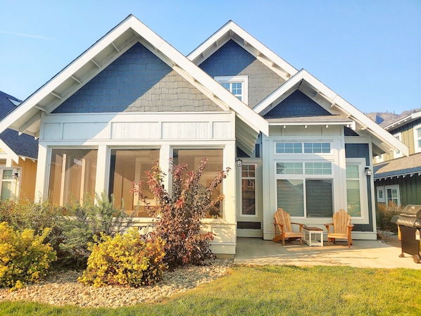 A modern two-story house with a large front porch, a covered patio, and a well-maintained garden.