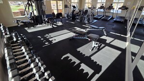 Ein Fitnessstudio mit verschiedenen Trainingsgeräten, großen Fenstern und Blick ins Freie.