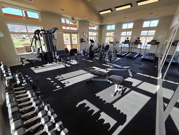 A gym with various exercise equipment, large windows, and a view of the outdoors.