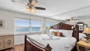 Ein Schlafzimmer mit einem großen Bett, einem Deckenventilator und Blick auf den Ozean durch die Fenster.