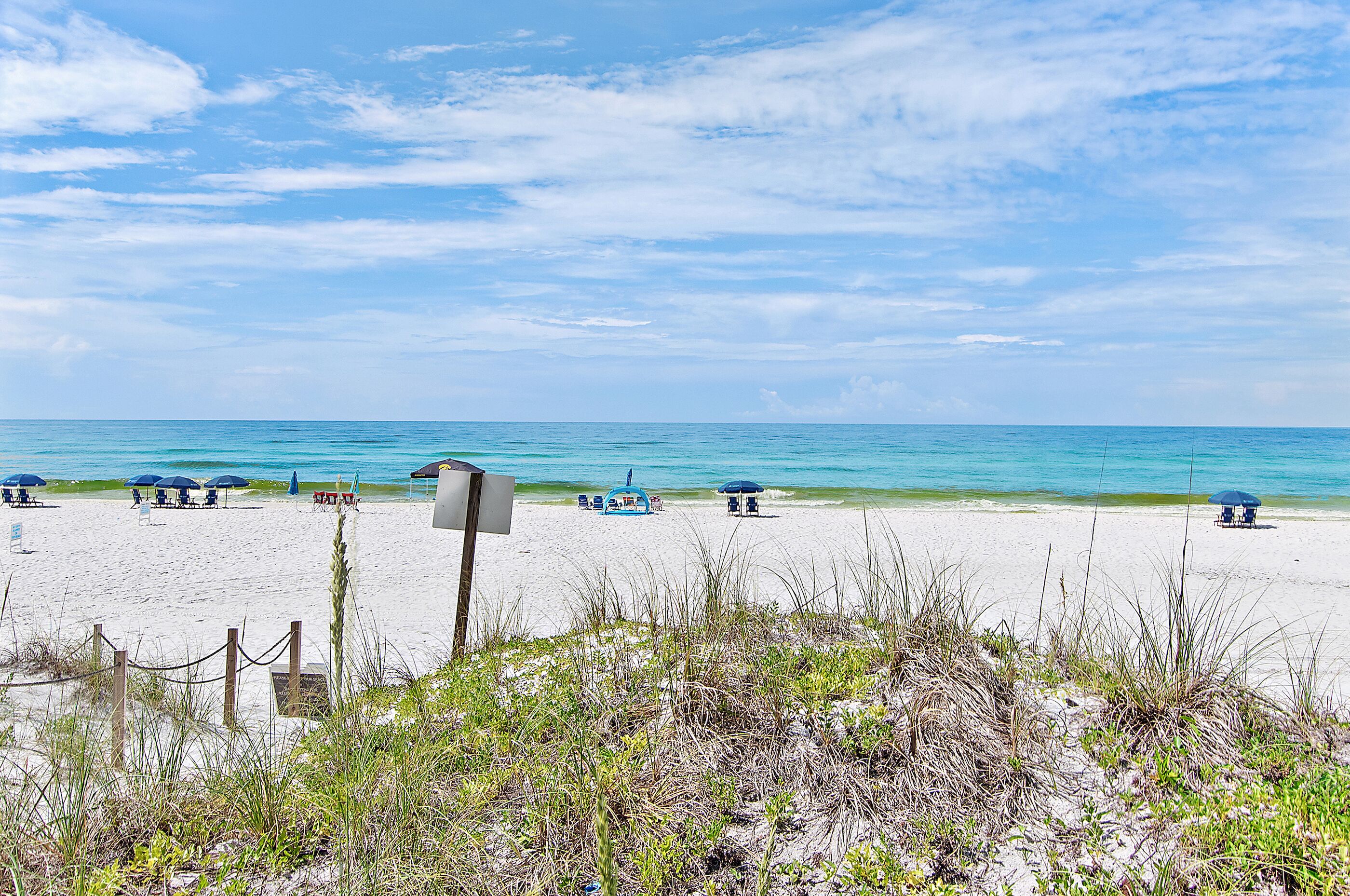 A beach with clear skies, a sandy shore, and several umbrellas.