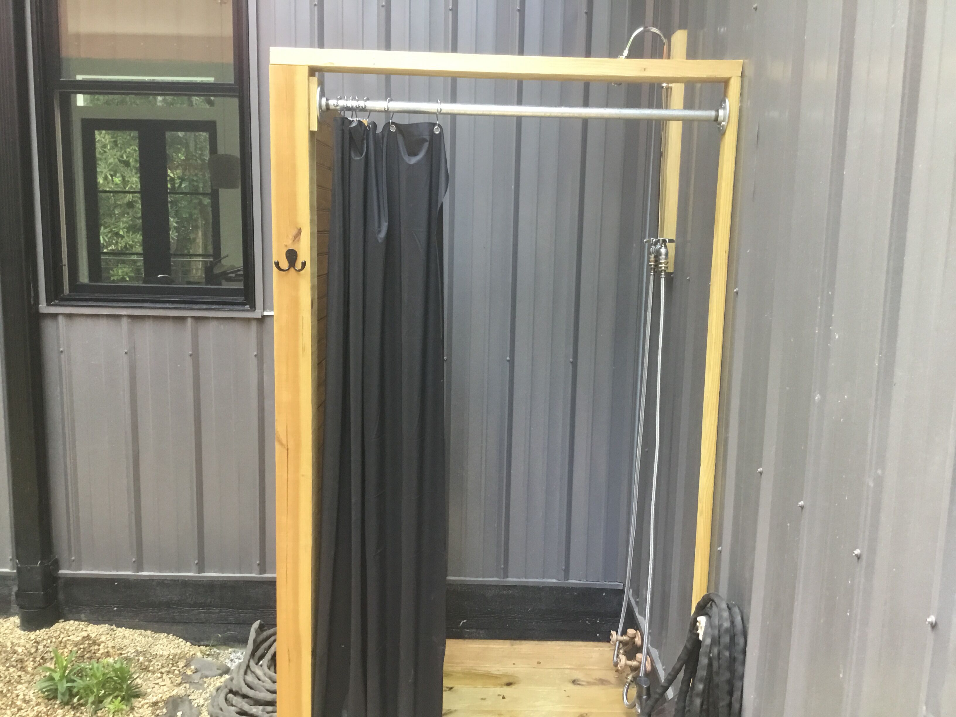 A wooden door with a black curtain, a metal showerhead, and a window with a view of trees.