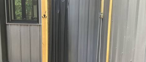 A wooden door with a black curtain, a metal showerhead, and a window with a view of trees.