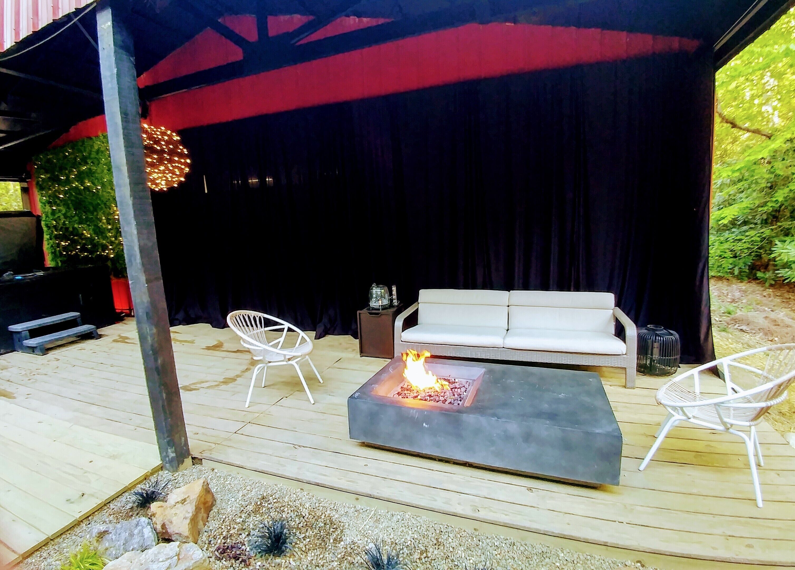 An outdoor patio with a fire pit, white sofa, and two white chairs.