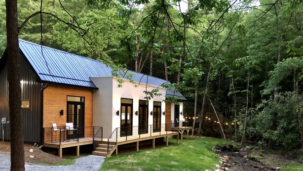 Una cabaña con techo de metal, terraza de madera y un arroyo que atraviesa la propiedad.