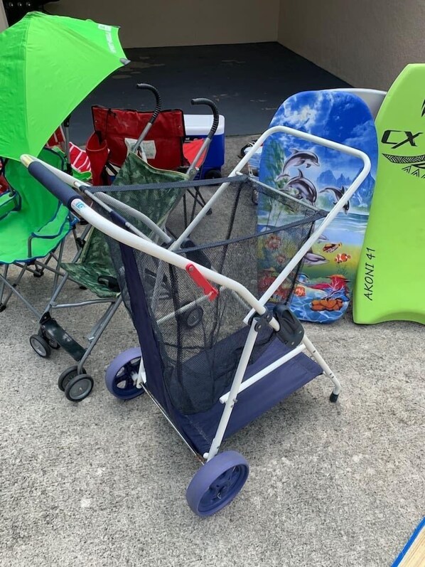 A baby stroller with a mesh canopy, a green umbrella, and a surfboard in the background.