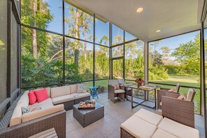 A spacious patio with wicker furniture, a dining table, and a view of a lush garden.