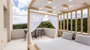 A bedroom with a bed, a small table, two chairs, and a view of greenery and hills.