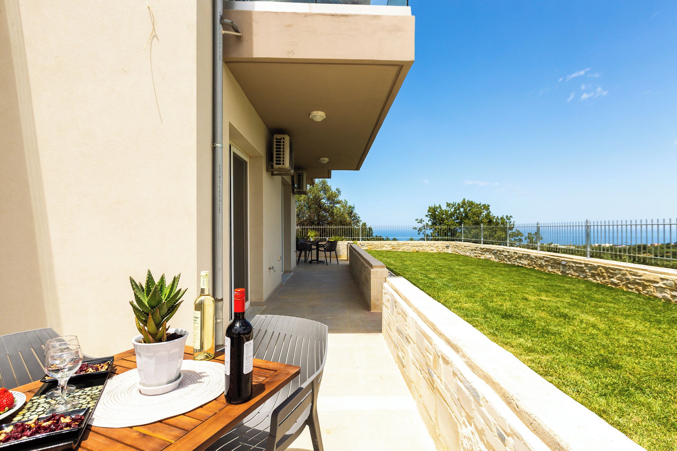 A balcony with a table set for dining, a potted plant, and a bottle of wine.