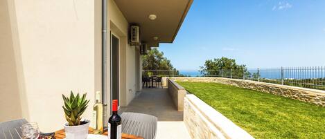 A balcony with a table set for dining, a potted plant, and a bottle of wine.