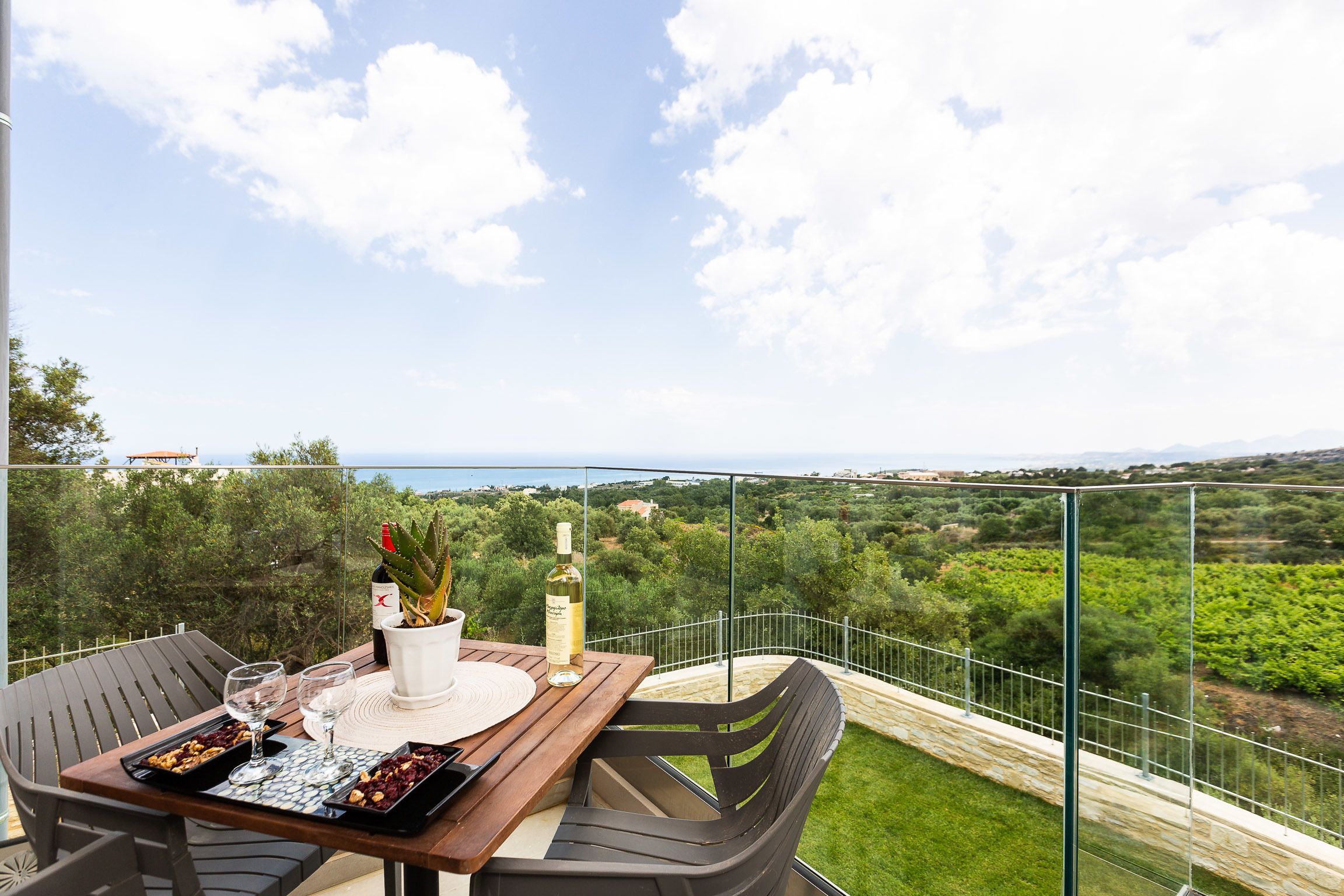 A balcony with a table set for two, featuring a bottle of wine, glasses, and a tray of nuts.