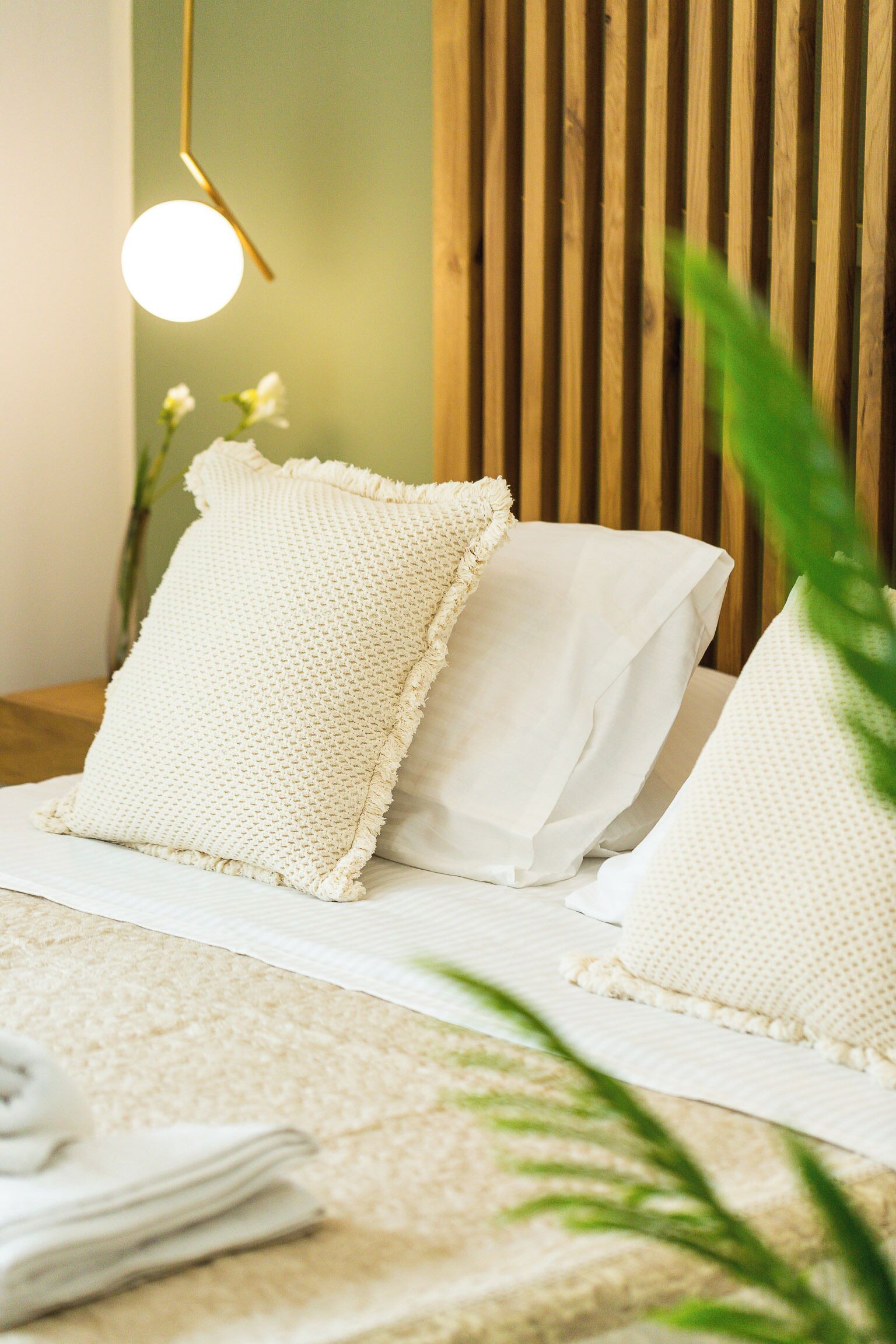 A neatly made bed with white bedding and a textured pillow, a hanging light fixture, and a wooden slat wall in the background.