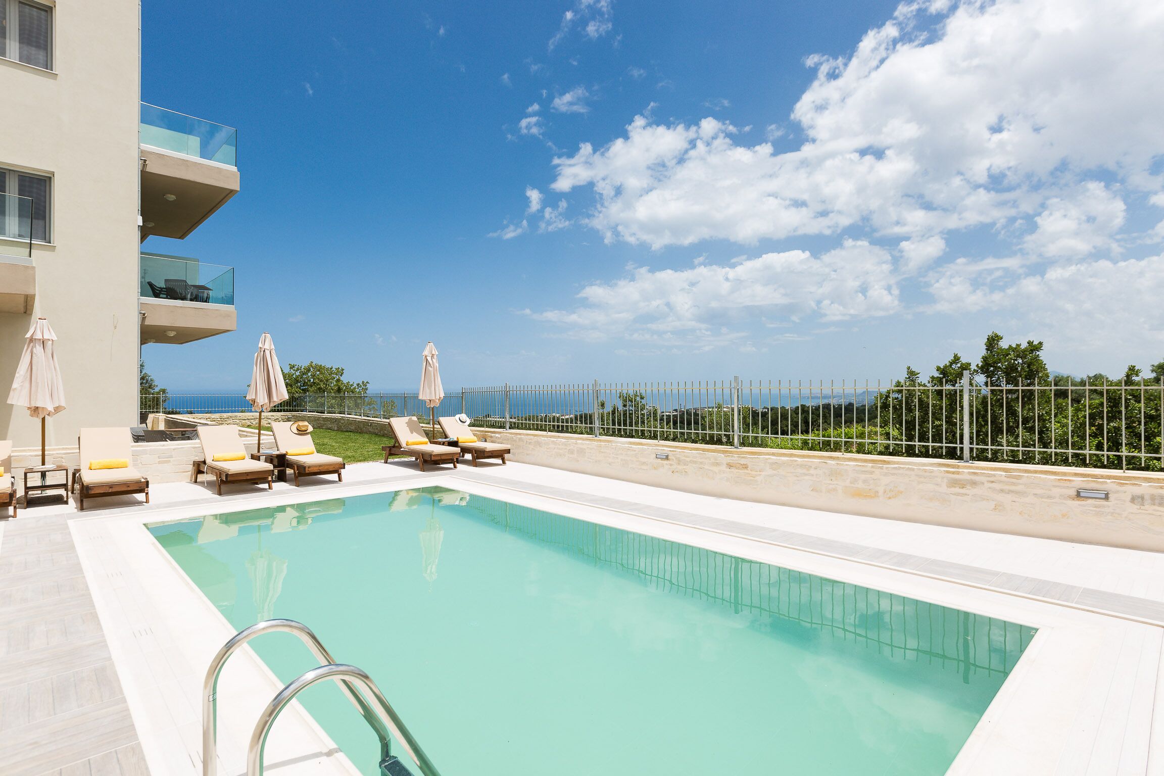 Una piscina con lettini e ombrelloni, cielo sereno e vista sul mare.