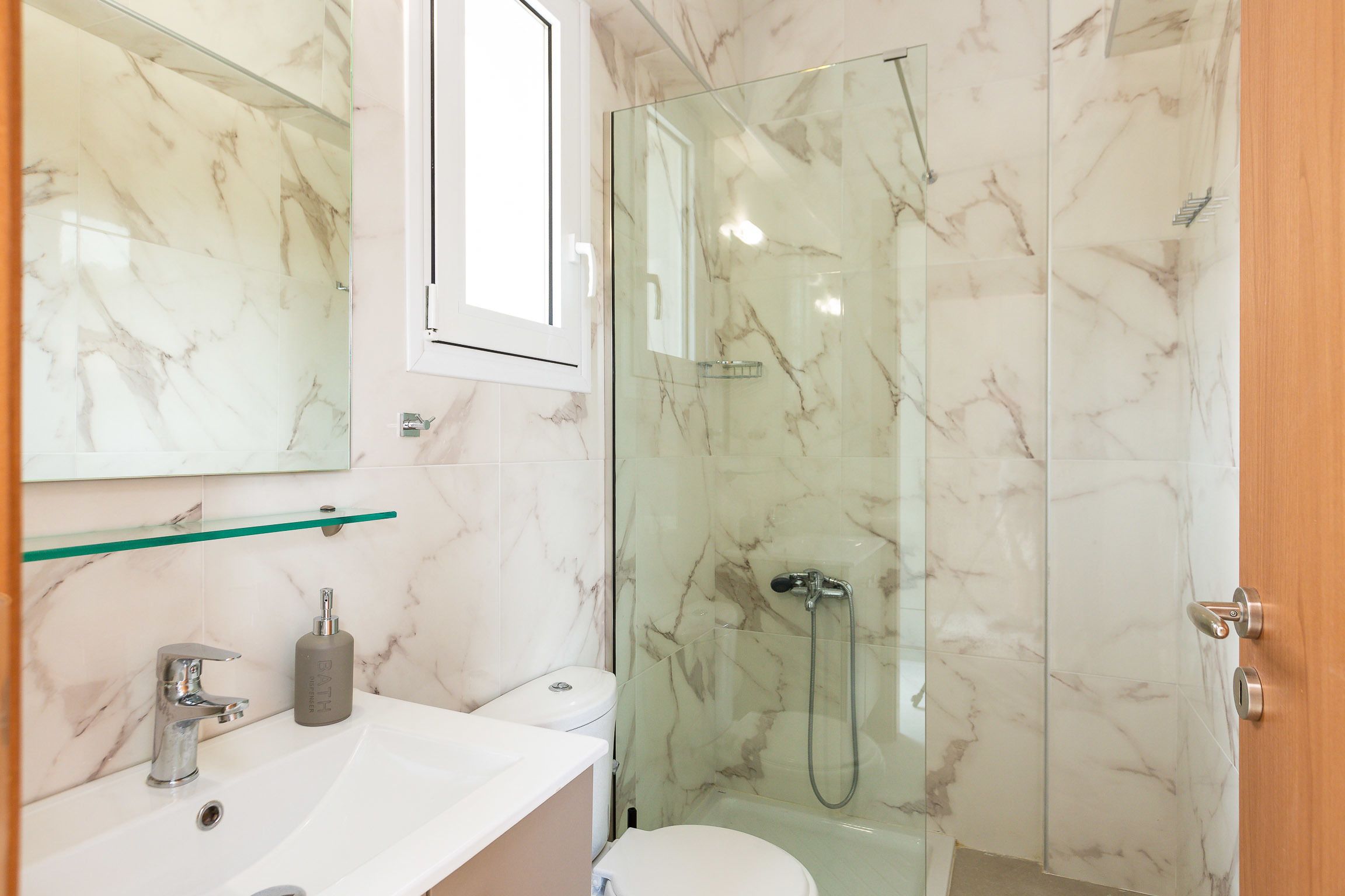 Une salle de bain avec une douche à parois de verre, un lavabo blanc doté d’un plan de toilette en marbre et des toilettes.