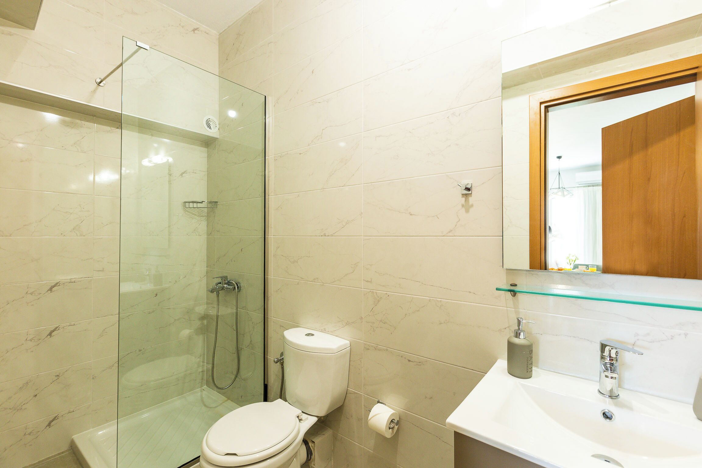 A bathroom with a glass-enclosed shower, a toilet, a sink with a mirror, and a glass shelf.