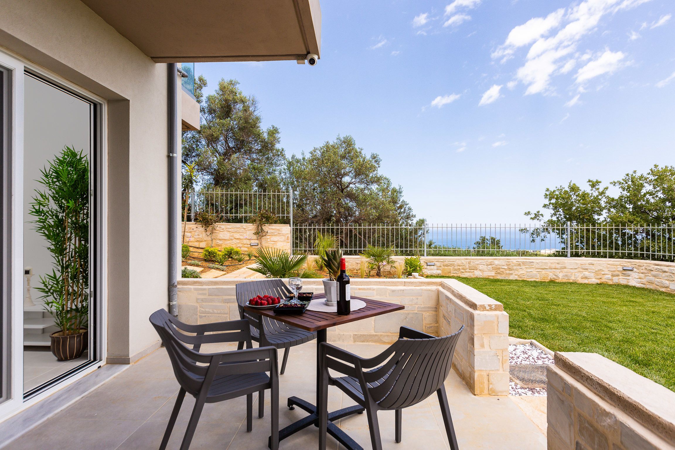 A patio with a table and chairs, a bottle of wine, and a bowl of fruit.