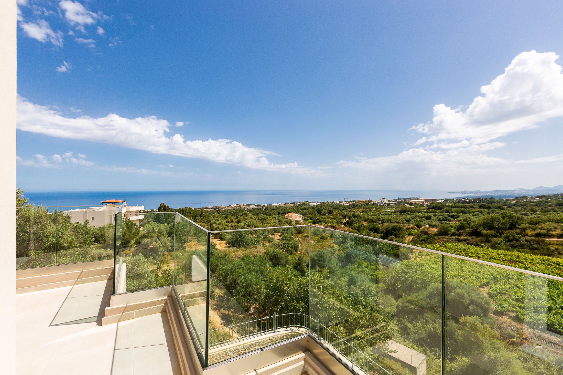 A balcony with a glass railing overlooking a vineyard and distant landscape.
