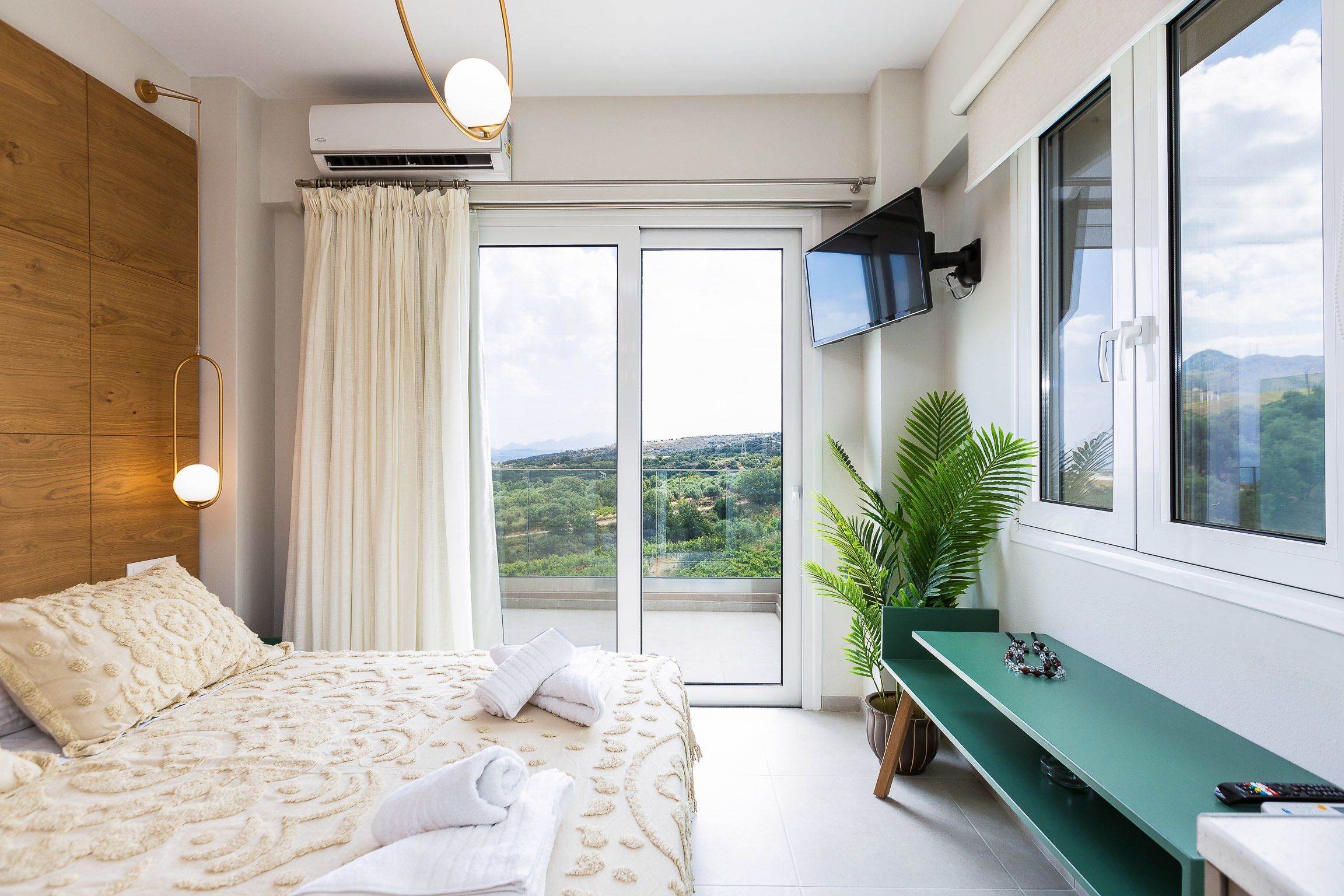 Ein Schlafzimmer mit einem Bett, einer grünen Bank, einem Fernseher und Blick ins Freie.