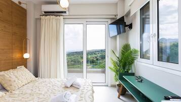 Ein Schlafzimmer mit einem Bett, einer grünen Bank, einem Fernseher und Blick ins Freie.