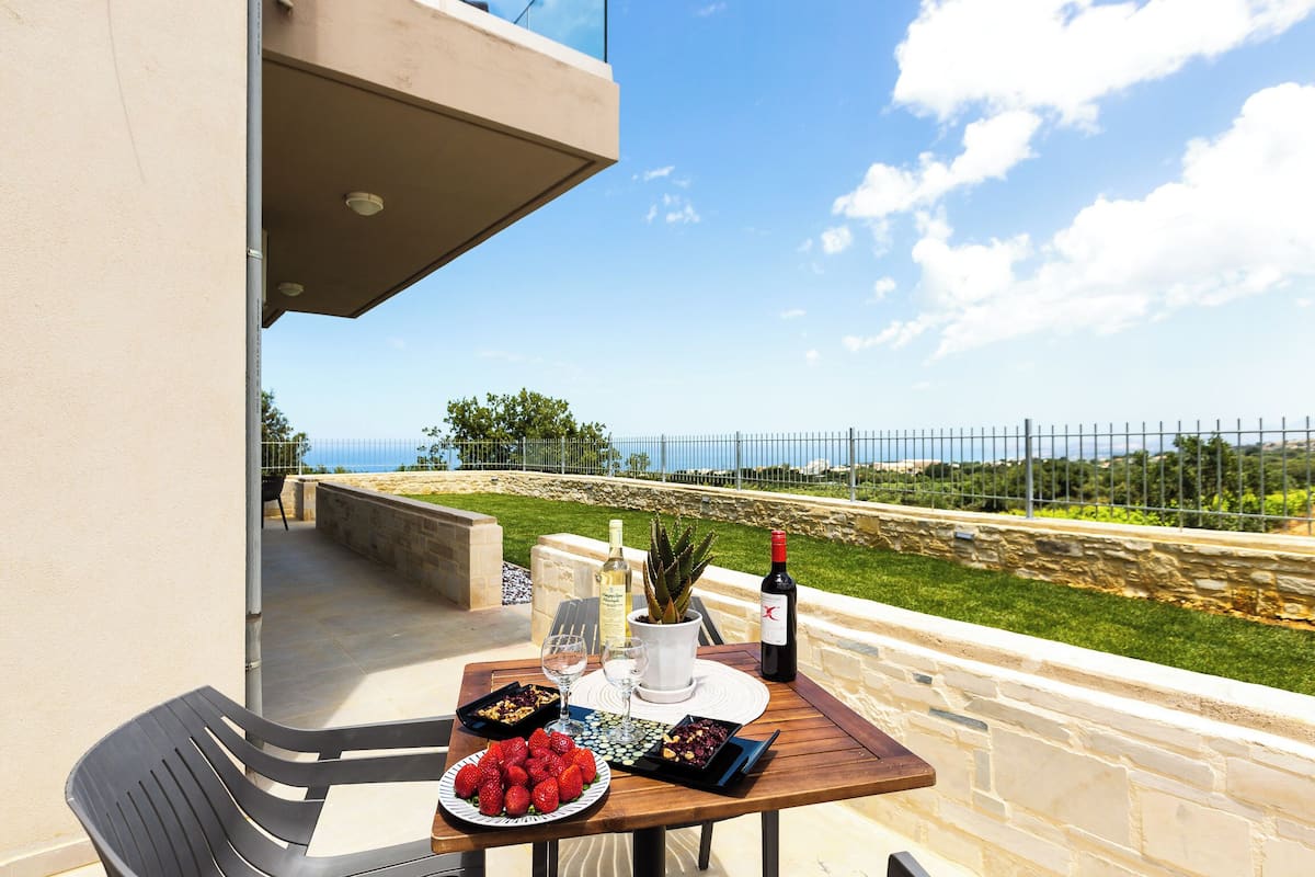 Ein Tisch auf einem Balkon mit schöner Aussicht, eine Weinflasche, eine Schale Erdbeeren und ein Blumentopf.