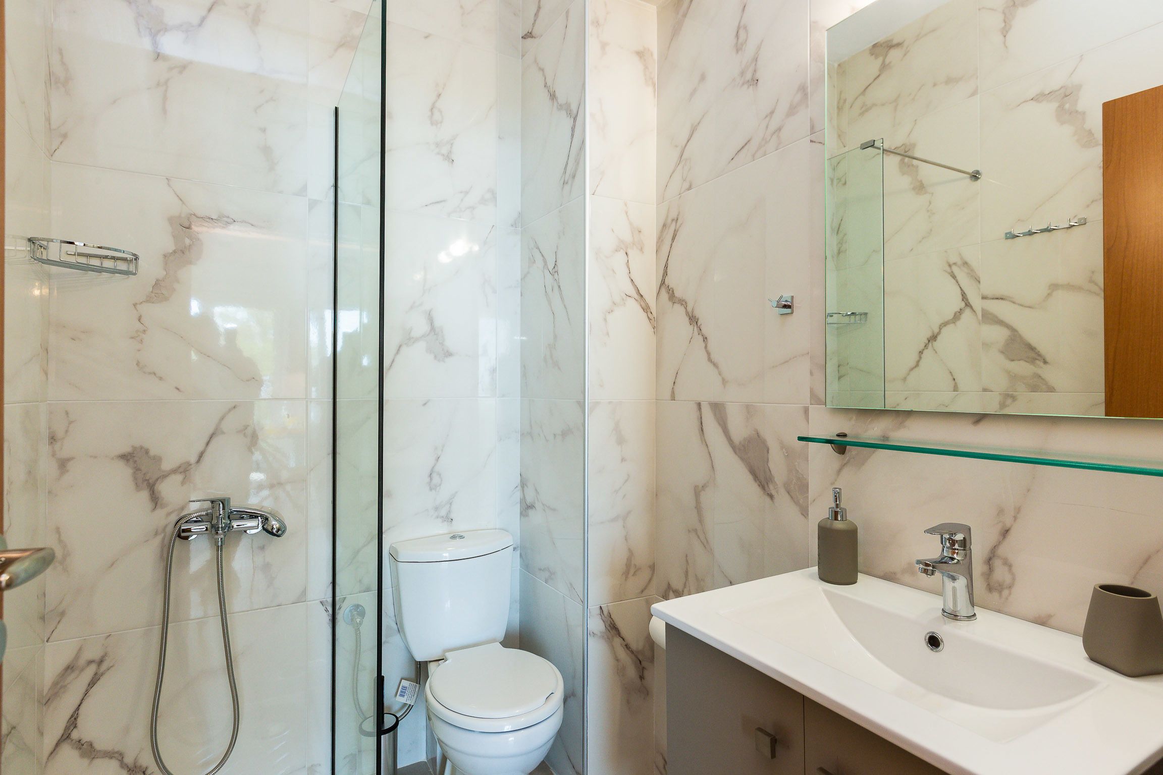 A bathroom with a glass-enclosed shower, a toilet, and a sink with a mirror above.