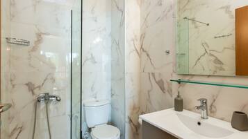 A bathroom with a glass-enclosed shower, a toilet, and a sink with a mirror above.