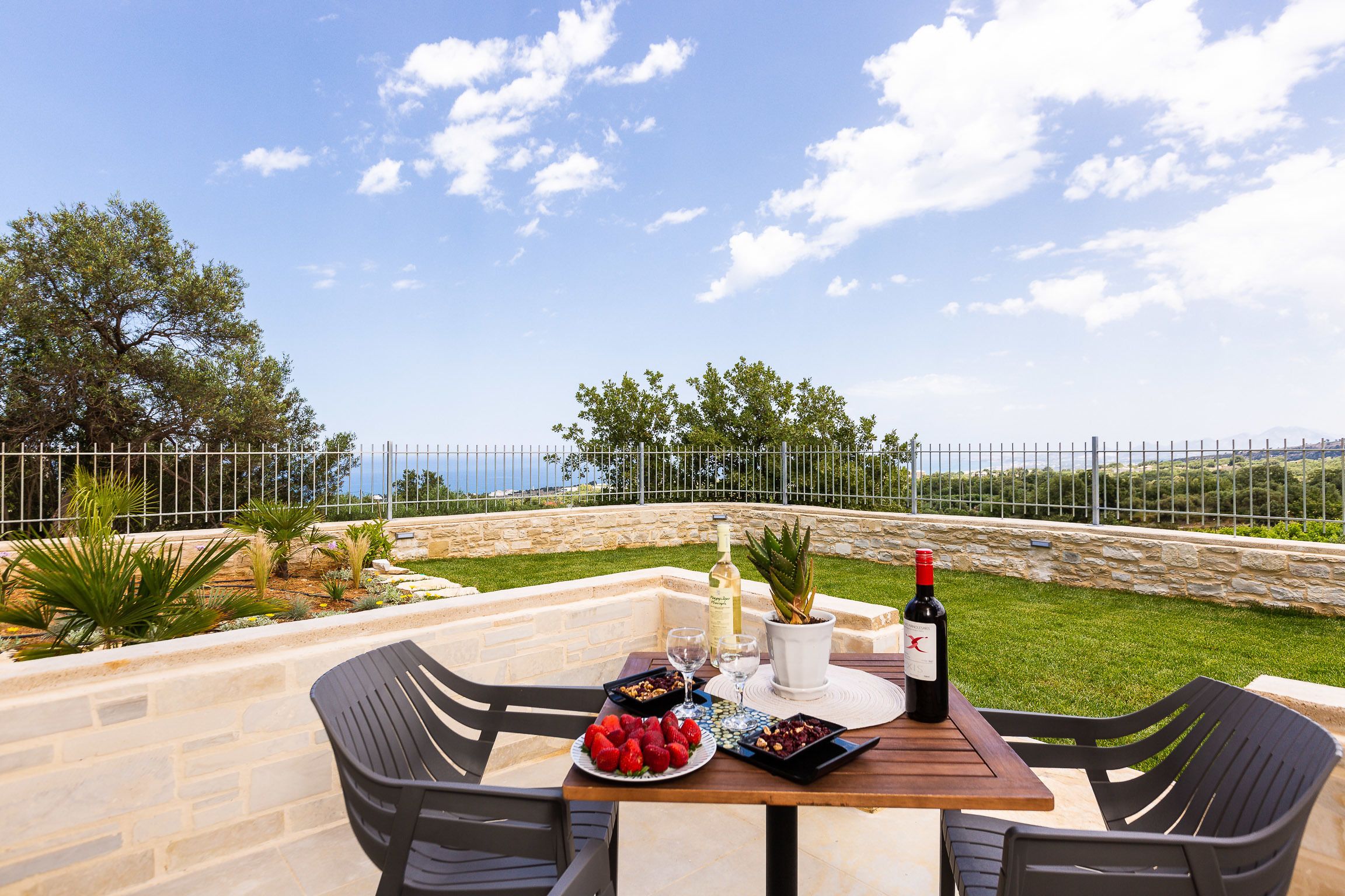 An outdoor dining area with a stone table, black chairs, and a view of the sea.