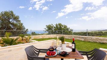 Un área de comedor al aire libre con una mesa de piedra, sillas negras y vistas al mar.