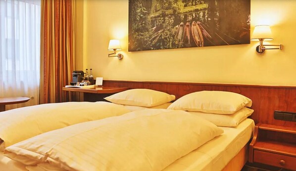 Una habitación de hotel con dos camas, un escritorio con lámpara y un cuadro en la pared.