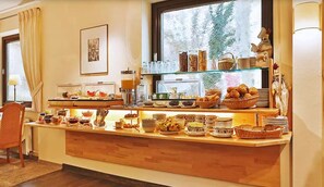 A breakfast buffet with various food items and beverages, a framed picture on the wall, and a window with a view of trees. - Hotel Am Kupferhammer (Tuebingen)