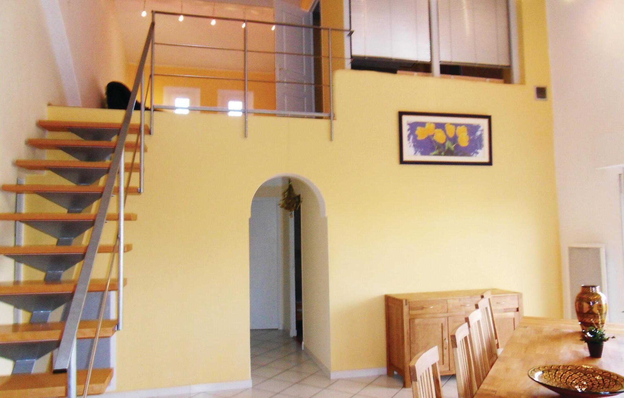 Un escalier menant à l’étage supérieur, un coin repas avec une table et des chaises, et un tableau encadré au mur.