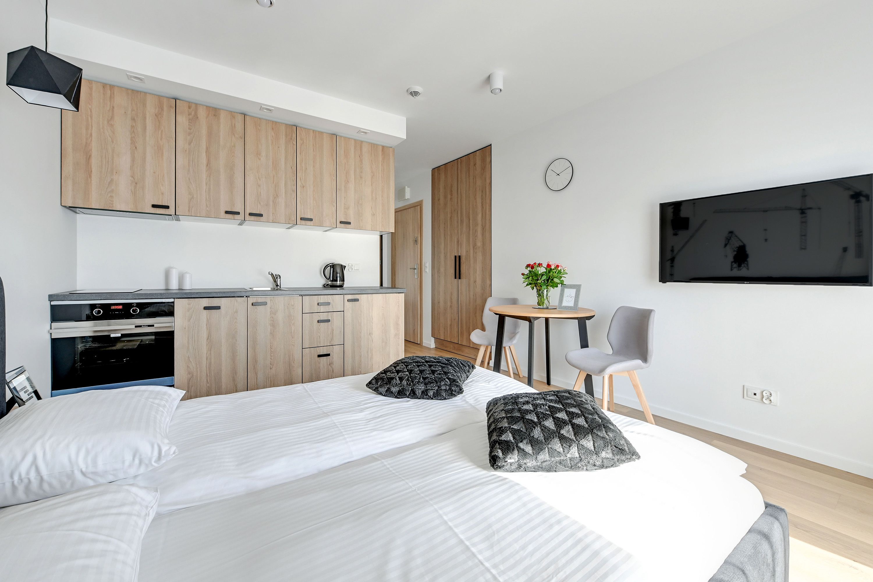 Ein modernes Hotelzimmer mit einem großen Bett, einer Küchenzeile, einem Essbereich und einem an der Wand befestigten Fernseher.