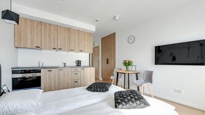 A modern hotel room with a large bed, a kitchenette, a dining area, and a wall-mounted TV. - Apartinfo Apartments Waterlane Island (Gdansk)