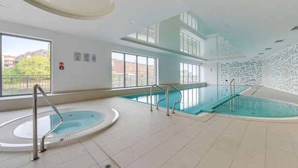 An indoor swimming pool with a hot tub, clear windows, and a view of buildings outside. - Apartinfo Apartments Waterlane Island (Gdansk)