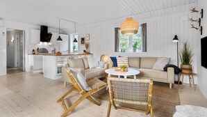 Un amplio espacio habitable con un sofá, dos sillones de mimbre, una mesa de centro redonda y un gran ventanal.