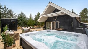 Un jacuzzi con cubierta de madera, sillas de descanso, una parrilla y una cabaña con techo inclinado.