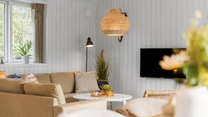 Una sala de estar con un sofá, una mesita redonda, un televisor y una lámpara colgante.