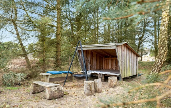 A rustic wooden cabin with a bench and a swing set in a forested area.