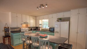 Een compacte keuken met witte kasten, een centraal eiland met stoelen, een kookplaat, magnetron en koelkast.