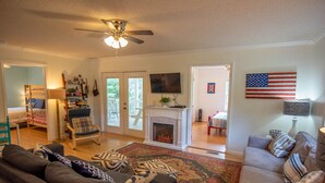 Een ruime woonkamer met een open haard, een plafondventilator en een grote Amerikaanse vlag.