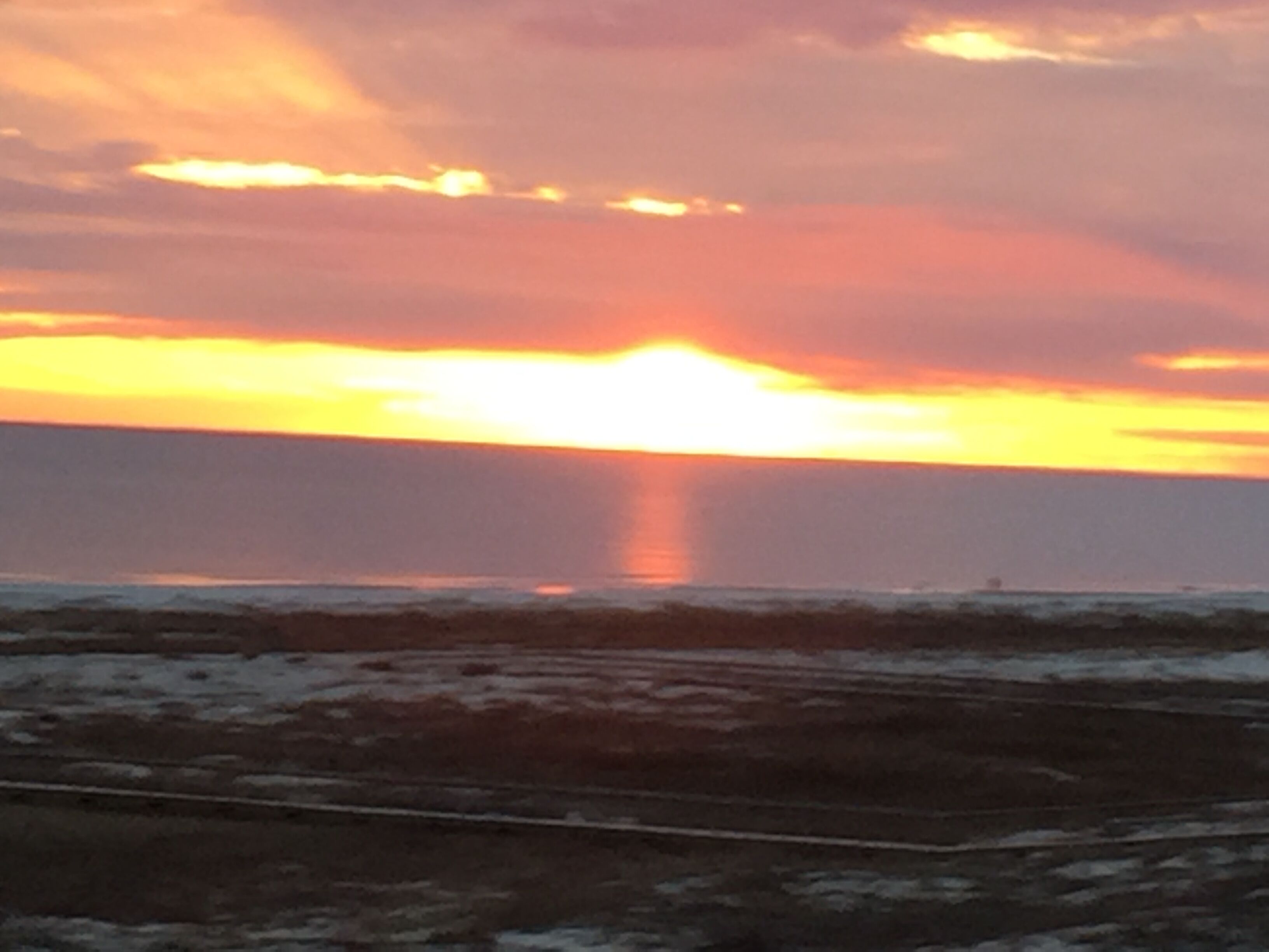 A sunset over a beach with a road in the foreground.