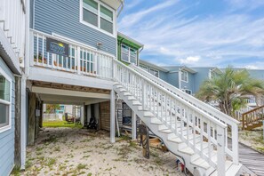 A beachfront property with a covered patio, a wooden deck, and a staircase leading to a balcony.