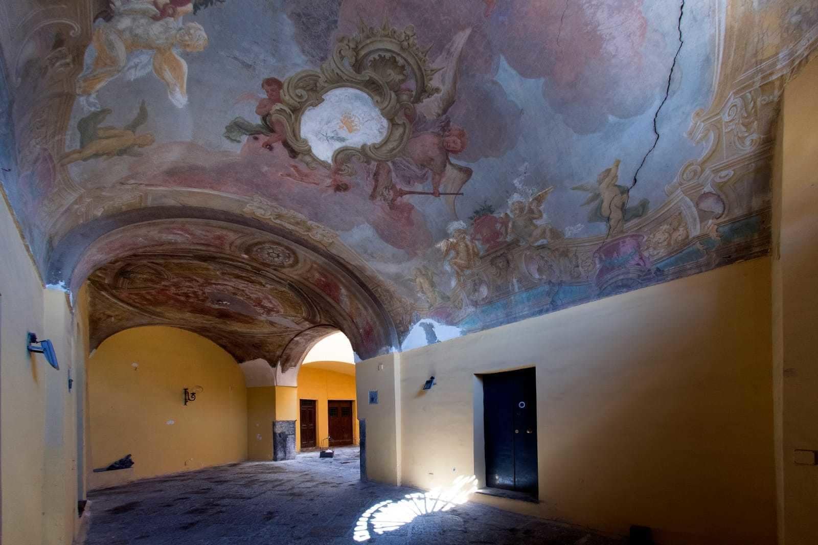 Un interior con techo alto, frescos ornamentados y un arco central que conduce a otra habitación.